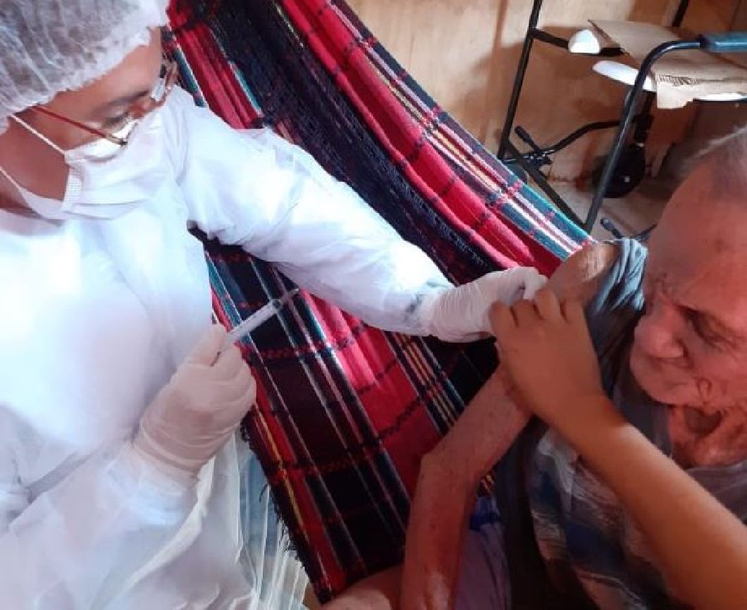 Deitado em uma rede, seu José recebe a dose de vacina contra a covid-19